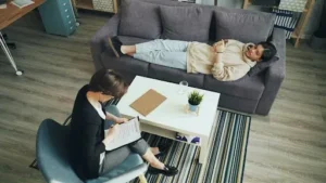 Woman lying on a couch during a psychiatric consultation with a therapist seated nearby