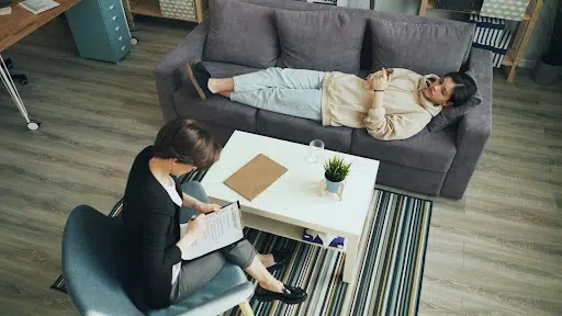 Woman lying on a couch during a psychiatric consultation with a therapist seated nearby