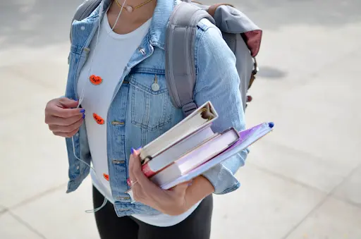 Student girl wearing a backpack, holding three books and a folder, ready for school