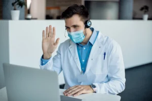 Male Nurse in a clinic waving during a video call on a laptop during Telemedicine