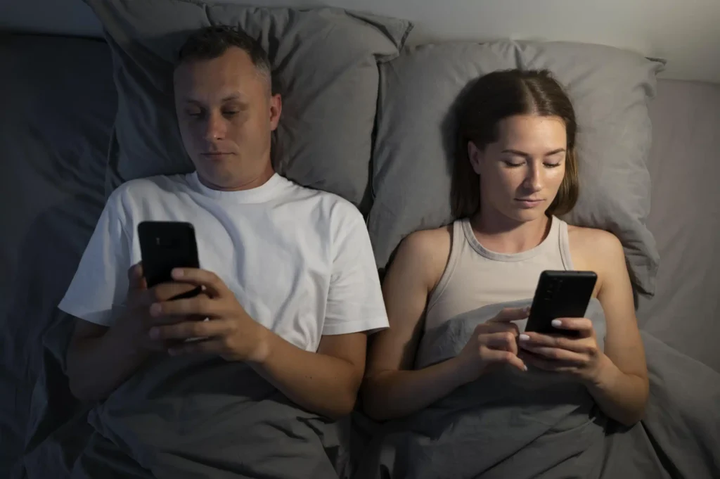Close-up of a couple lying in bed, both using their smartphones